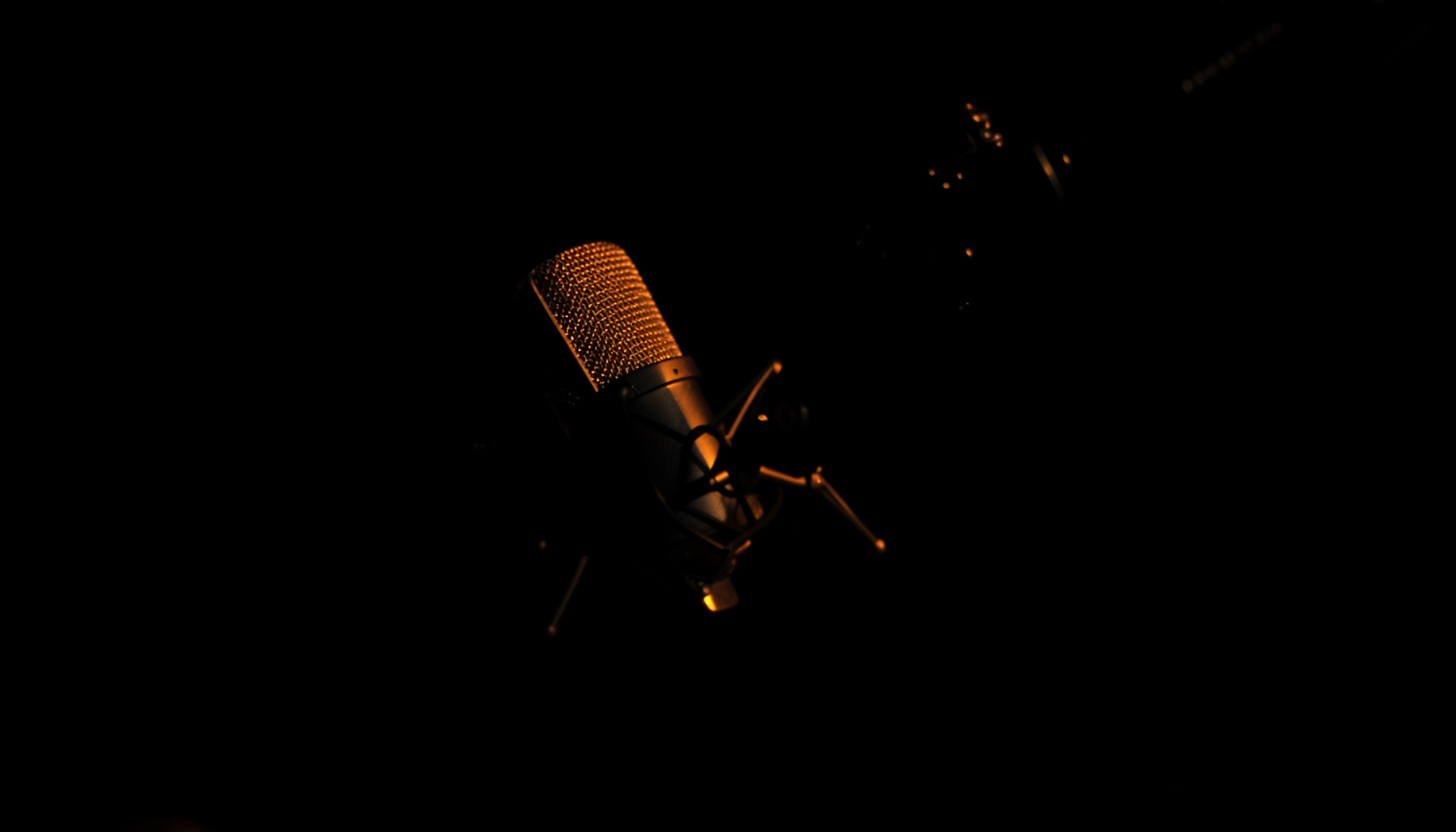 Dark atmospheric photograph of a studio microphone on a boom arm, deep shadows with subtle warm amber glow on the mic grille