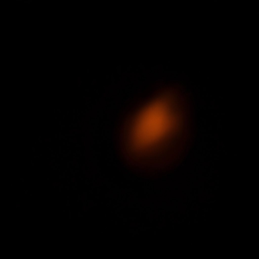 A dark close-up photograph of a virtual reality headset lens with subtle orange reflections against a near-black backdrop