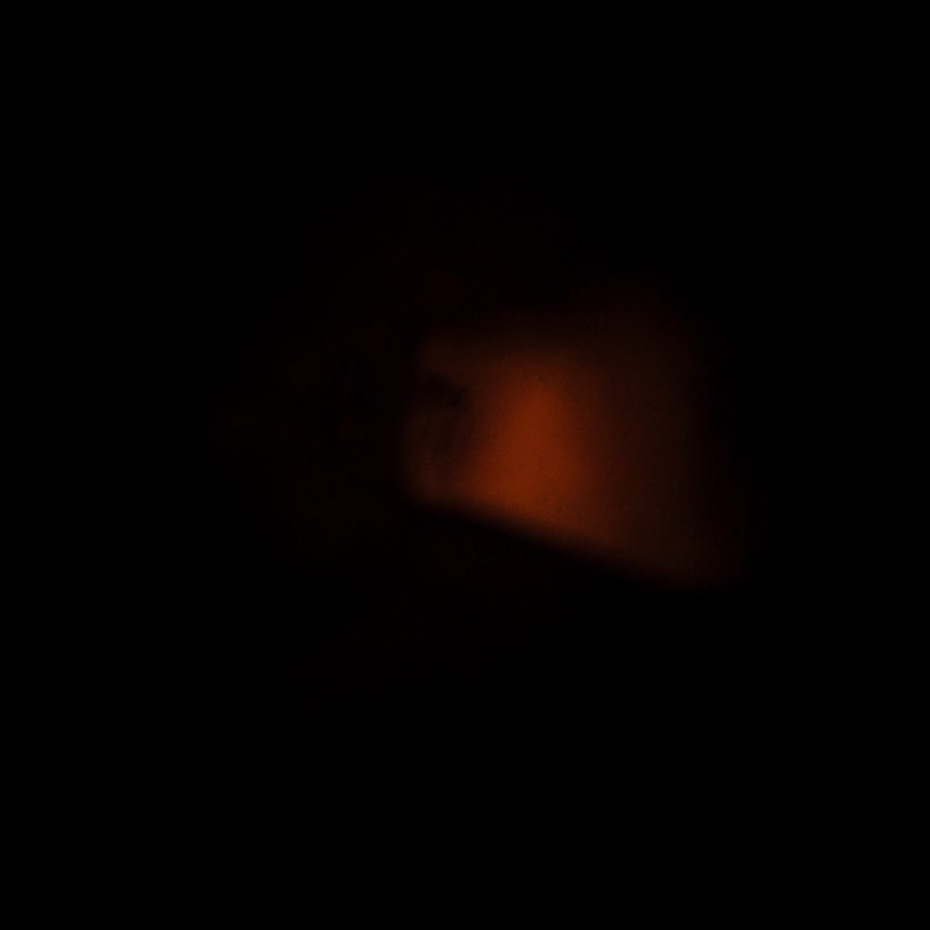 A dark, low-key photograph of a virtual reality headset in deep shadow with a soft orange rim light along one edge