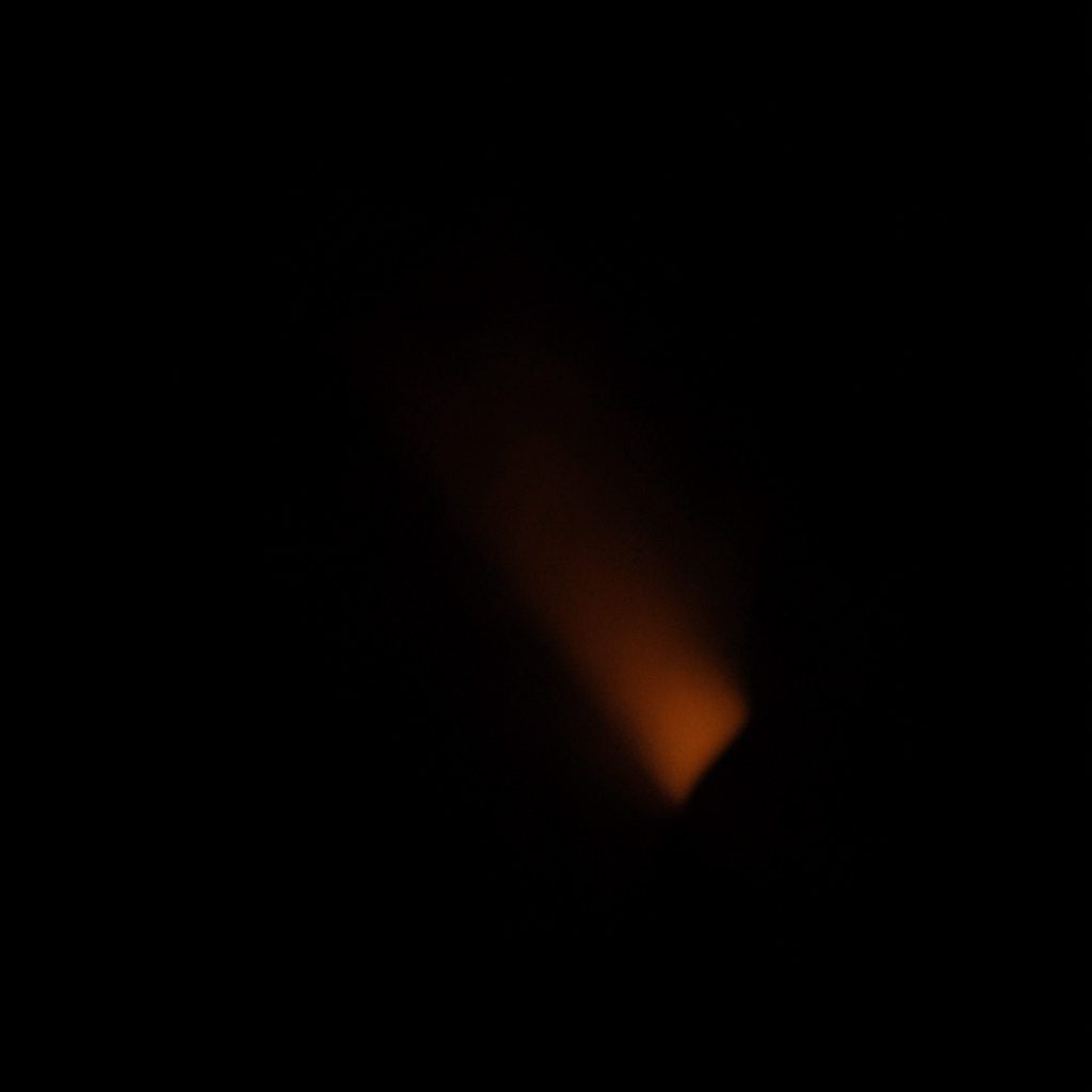 A dark atmospheric photograph of a virtual reality headset against a near-black charcoal background with a subtle warm orange glow