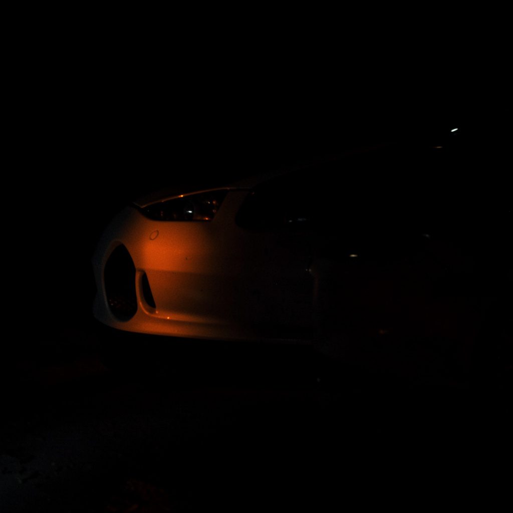 A dark, moody close-up photograph of a virtual reality headset resting in deep shadow, with faint orange highlights catching the edges against a near-black background