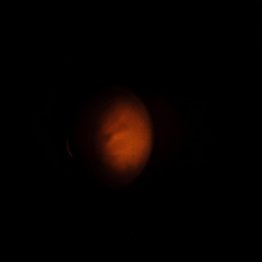 A wide, dark atmospheric photograph of a virtual reality headset and controller sitting in low shadowy light with a muted charcoal and orange toned background